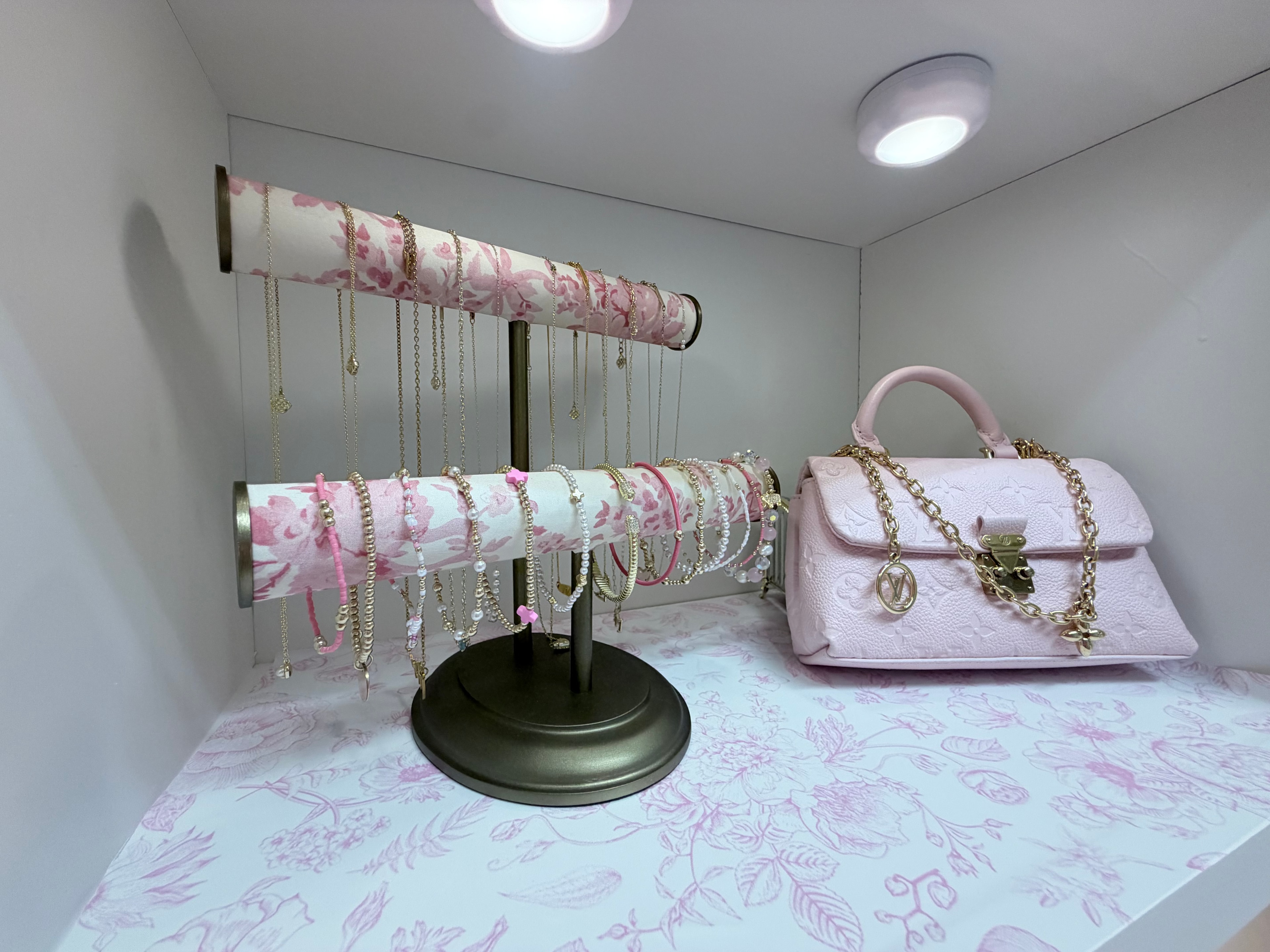 Jewelry stand with gold necklaces and pink Louis Vuitton bag on floral shelf liner